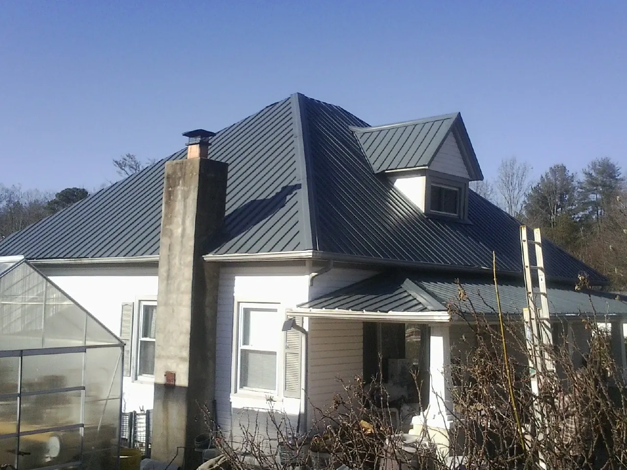 Dark blue standing seam metal roof on a white farmhouse with dormer — Slate & Tile Roof Repair by Roofing Brothers in Palm