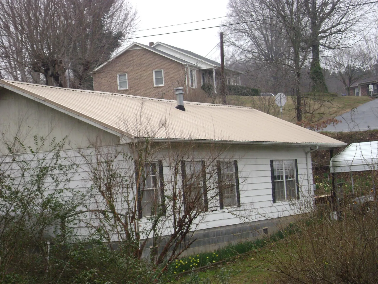 Tan metal roof on a white sided house set into a hillside — Commercial Roofing by Roofing Brothers in Palm